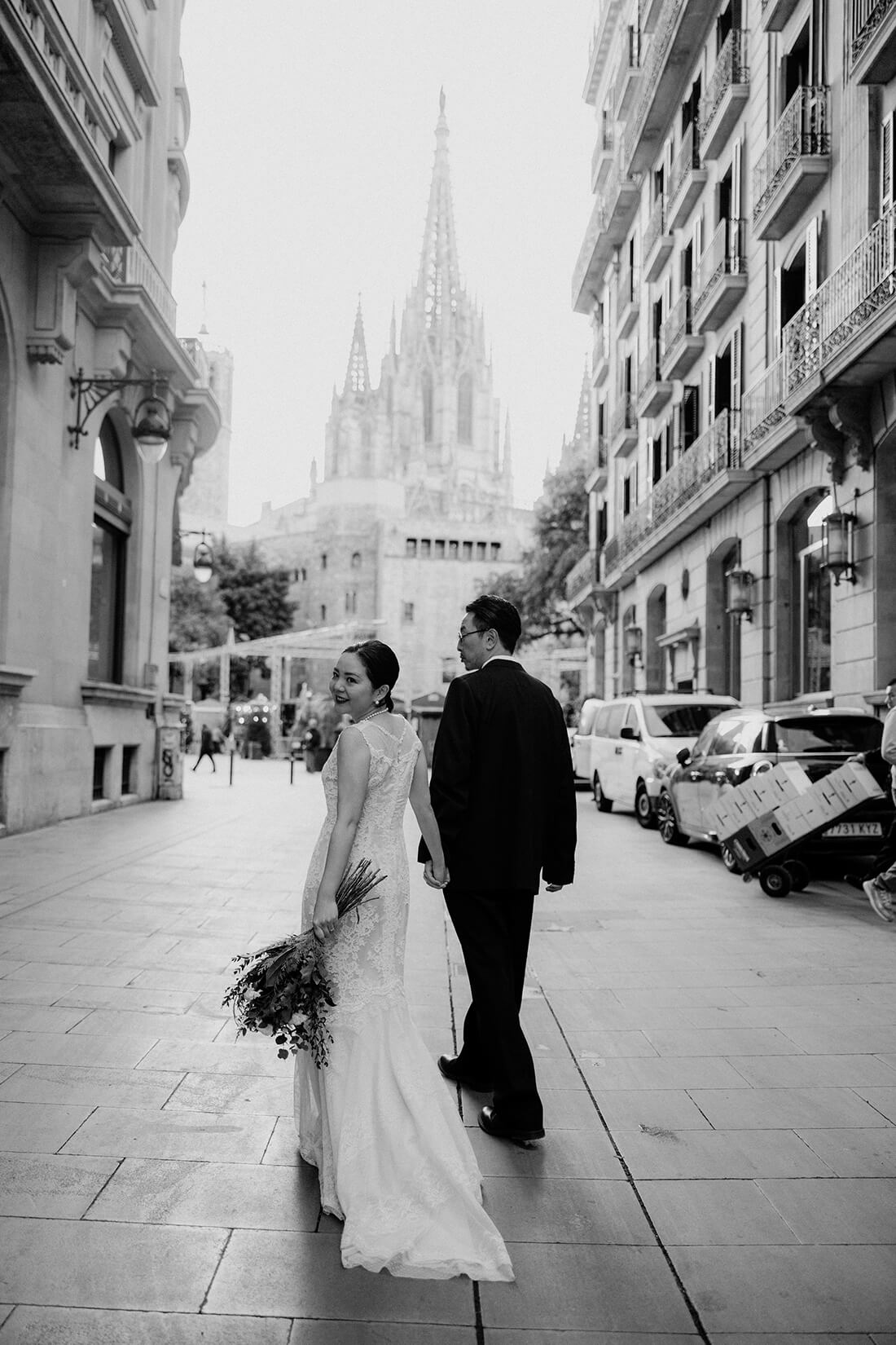 荘厳なバルセロナ大聖堂を背に、優雅に佇む新郎新婦のタイムレスなモノクロ写真。ゴシック様式の建築美と光影が織りなす、映画のワンシーンのようなドラマチックなウェディングフォト。数十年後も見返したくなる、芸術的で洗練されたバルセロナの前撮り事例。