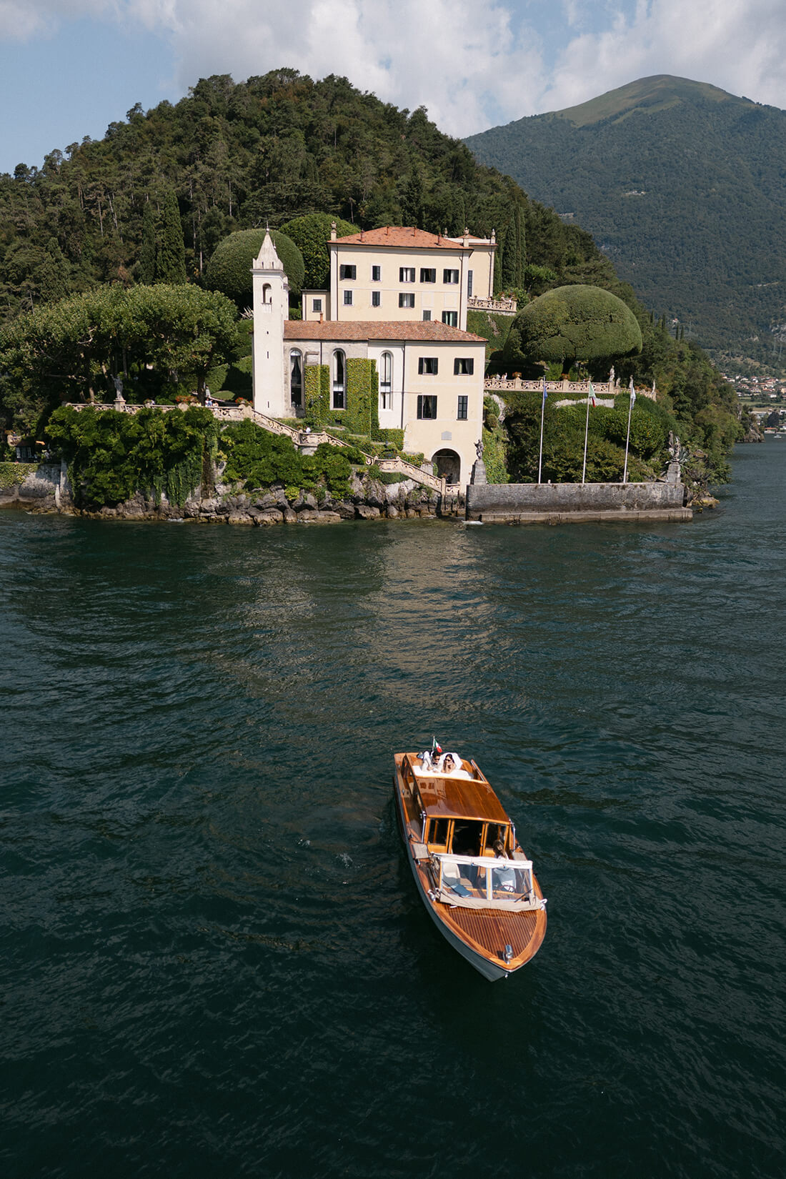 木製プライベートボートからコモ湖の街並みと山々の絶景を眺める新郎新婦の後ろ姿（イタリア海外挙式・前撮りプラン）| Totte
