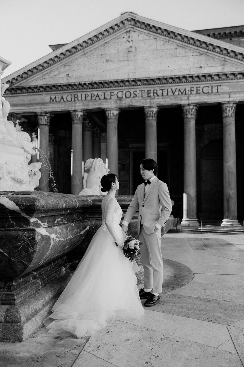 ローマの古代遺跡パンテオン（Pantheon）の前、人影のない静寂な広場に二人きりで佇む新郎新婦のモノクロ写真。2000年の歴史を刻む巨大な柱と、タイムレスな世界観が調和した、ELLE研修修了プランナー監修・Totteのドラマチックで希少な早朝フォトウェディング・前撮り。
