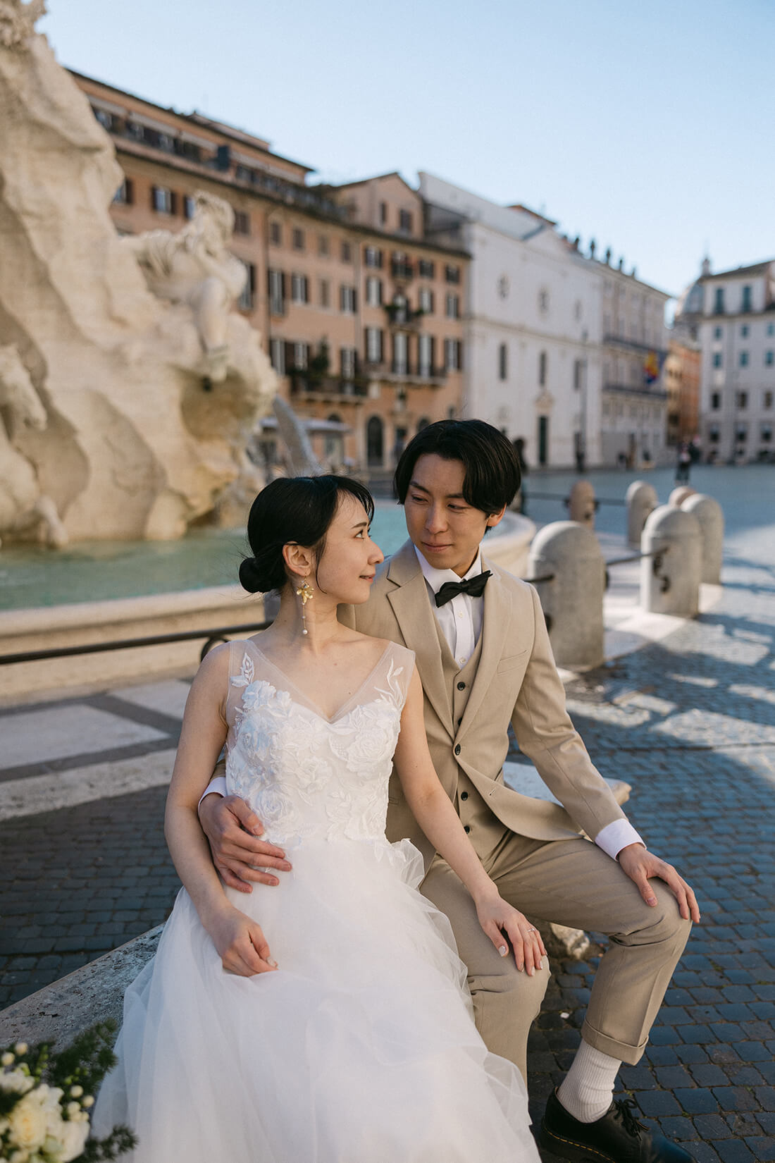 ローマで最も美しい広場の一つ、ナヴォーナ広場（Piazza Navona）の中央にあるベルニーニ作「四大河の噴水」の前で、楽しげに笑顔を見せる新郎新婦。バロック建築に囲まれた華やかなロケーションで、芸術と歴史を感じながら自然体で過ごす、ELLE研修修了プランナー監修・Totteのフォトウェディング・ハネムーン撮影。