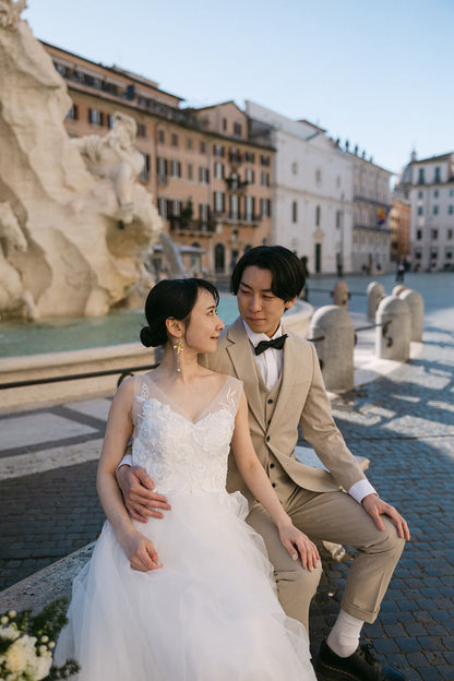 ローマで最も美しい広場の一つ、ナヴォーナ広場（Piazza Navona）の中央にあるベルニーニ作「四大河の噴水」の前で、楽しげに笑顔を見せる新郎新婦。バロック建築に囲まれた華やかなロケーションで、芸術と歴史を感じながら自然体で過ごす、ELLE研修修了プランナー監修・Totteのフォトウェディング・ハネムーン撮影。