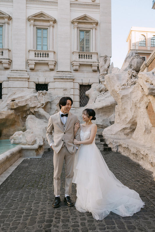 ローマの象徴「トレビの泉（Fontana di Trevi）」のダイナミックな彫刻を背景に、笑顔で腕を組む新郎新婦。バロック芸術の傑作と水の音が聞こえてきそうな臨場感あふれるロケーションで、ELLE研修修了プランナー監修・Totteが切り取る、楽しげでドラマチックなフォトウェディング・ハネムーン撮影。