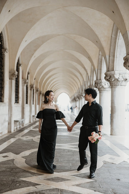 イタリア・ベネチアのドゥカーレ宮殿（Palazzo Ducale）の回廊にて、連続する美しいアーチの下を手をつなぎ優雅に歩く新郎新婦。ゴシック様式の建築美と光のコントラストが印象的な、ELLE研修修了プランナー監修・Totteの洗練されたフォトウェディング・前撮り写真。