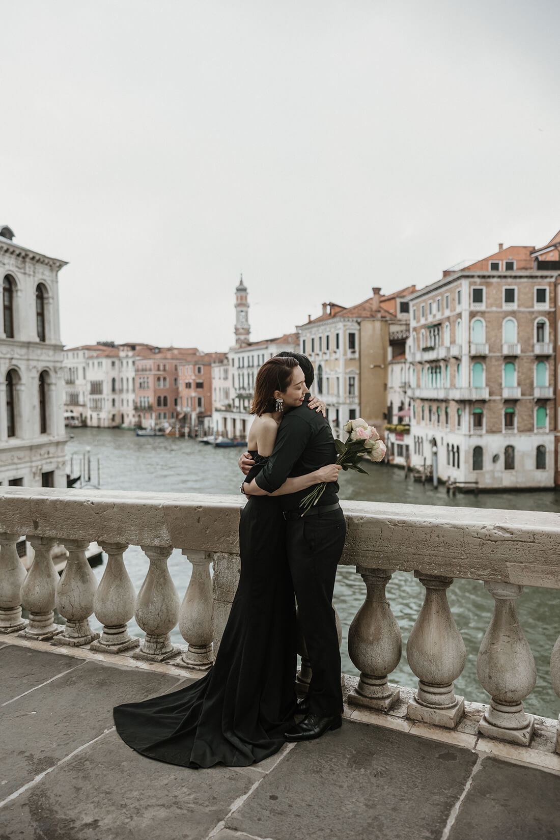 イタリア・ベネチアの象徴であるリアルト橋（Ponte di Rialto）の上で、大運河（カナル・グランデ）の絶景を背景に情熱的に抱き合う新郎新婦。活気ある運河の風景と二人の世界を対比させた、ELLE研修修了プランナー監修・Totteのドラマチックなフォトウェディング・ハネムーン撮影。